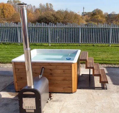 Уличная квадратная купель с дровяной печью на фоне металлического забора